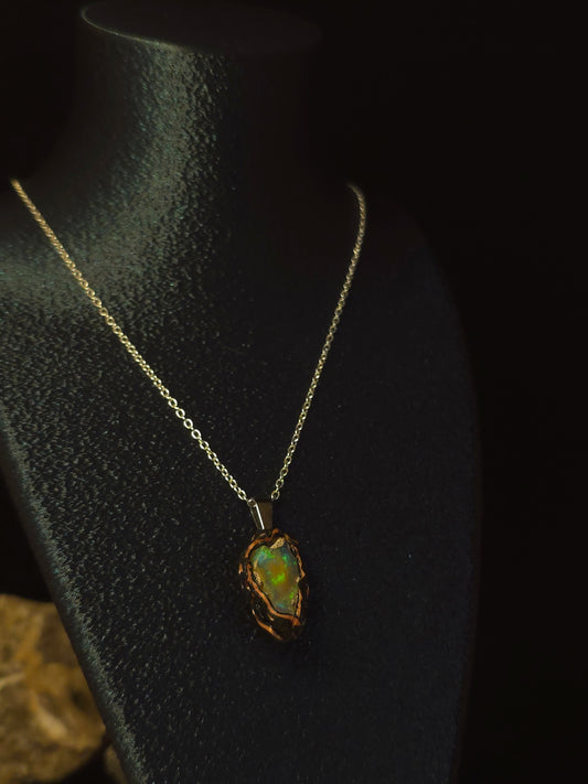 A gold chain necklace with a raw, irregular opal pendant displayed on a black jewelry bust against a dark background.
