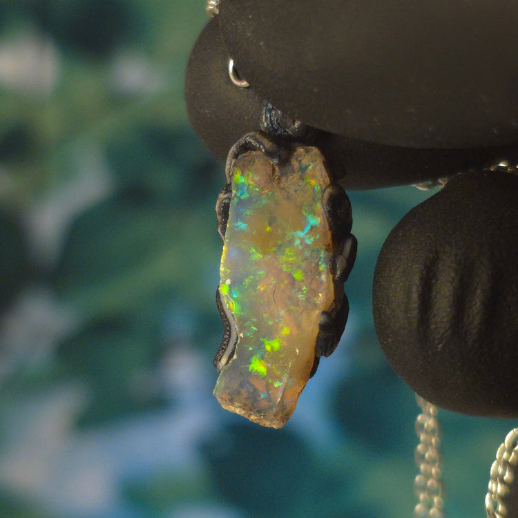 Video: raw uncut Ethiopian Welo opal pendant. Colour: blue and green, vivid. Body: transparent. Held in a gloved hand against a dark background.