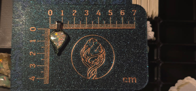 Raw uncut Ethiopian Welo opal pendant. Colour: red, green, vivid. Body: duotone blue/white. Placed next to a steel ruler for scale.