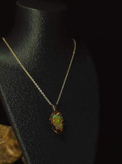 A gold chain necklace with a raw, irregular opal pendant displayed on a black jewelry bust against a dark background.