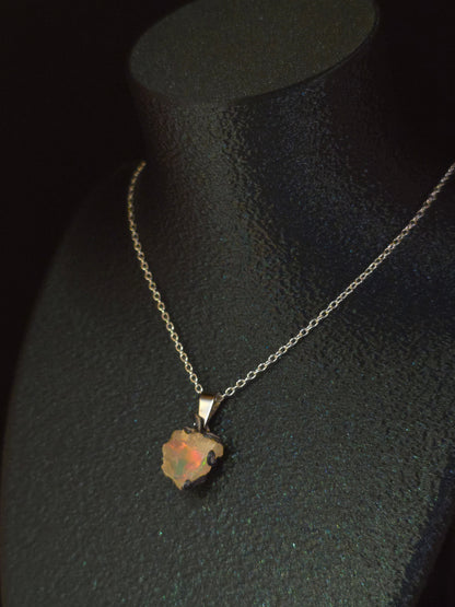 A delicate silver chain necklace with a small, irregularly shaped opal pendant, displayed on a black velvet jewelry bust.