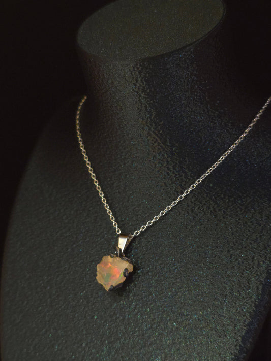 A delicate silver chain necklace with a small, irregularly shaped opal pendant, displayed on a black velvet jewelry bust.