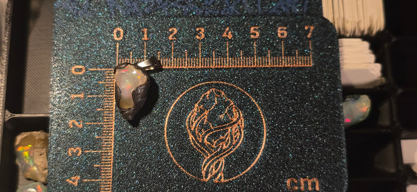Raw uncut Ethiopian Welo opal pendant with gold & red fire, white heart. Placed next to a steel ruler for scale.