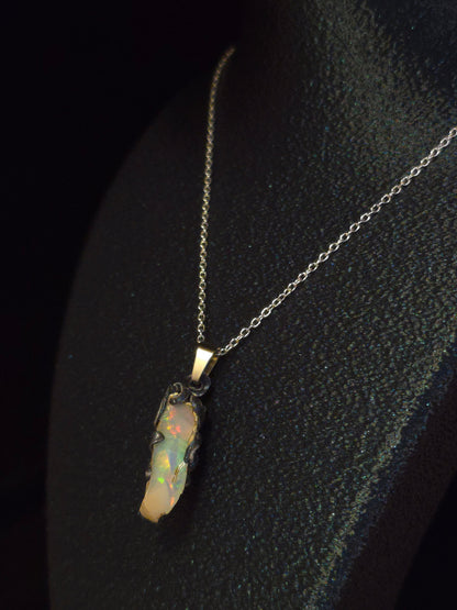 A silver chain necklace with a small pendant featuring a colorful opal stone, displayed on a black textured surface.