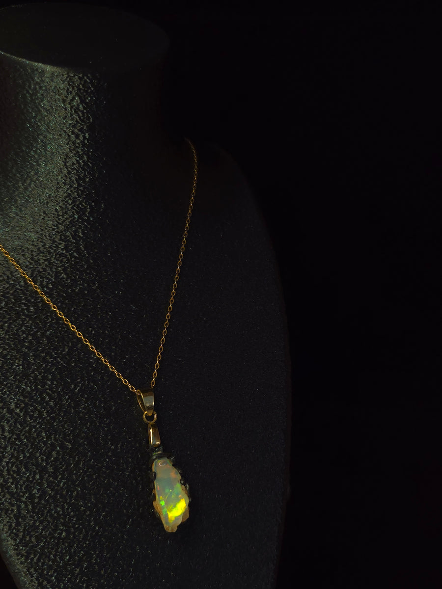 Raw uncut Ethiopian Welo opal pendant, green flashes on light blue. Worn on a black display bust.