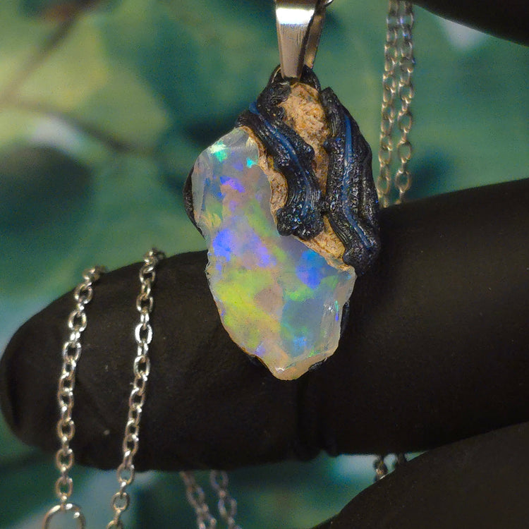 Video: raw uncut Ethiopian Welo opal pendant. Colour: blue, teal, with green hints, moderate. Body: light blue. Held in a gloved hand against a green background.