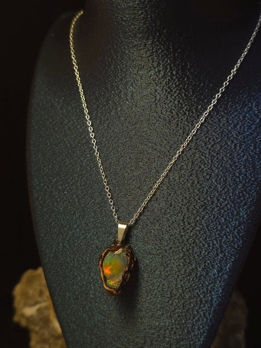 A silver chain necklace with a raw, irregular opal pendant displayed on a black textured mannequin bust against a dark background.