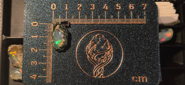Raw uncut Ethiopian Welo opal pendant with green flashes & blue hues. Placed next to a steel ruler for scale.