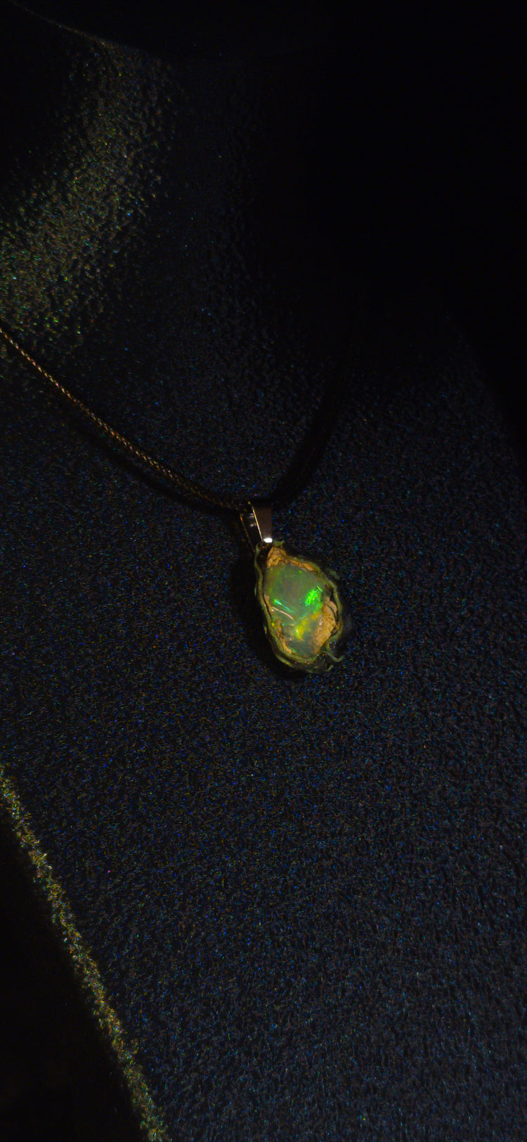 Raw uncut Ethiopian Welo opal pendant. Colour: green and blue, strong. Body: clear, light blue. Worn on a black display bust.