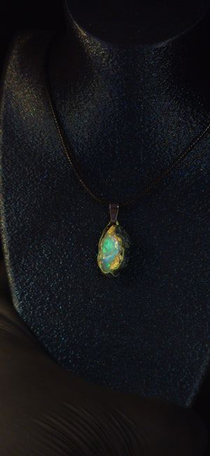 Raw uncut Ethiopian Welo opal pendant. Colour: green and blue, strong. Body: clear, light blue. Worn on a black display bust.